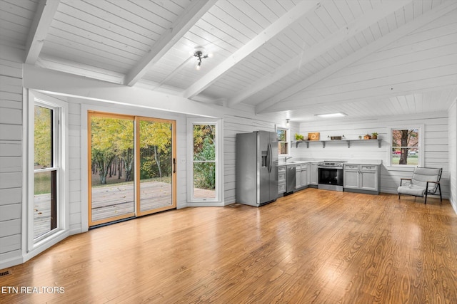 unfurnished living room featuring vaulted ceiling with beams, wood walls, plenty of natural light, and light hardwood / wood-style floors