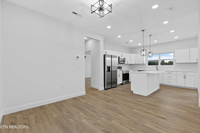 kitchen with appliances with stainless steel finishes, light wood-type flooring, decorative light fixtures, a center island, and white cabinetry