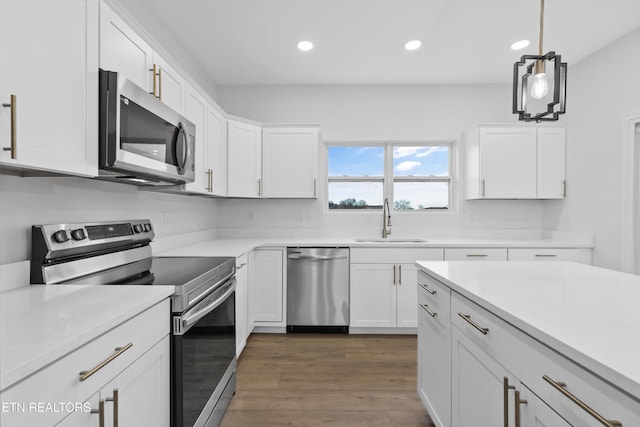 kitchen featuring appliances with stainless steel finishes, sink, white cabinets, dark hardwood / wood-style floors, and hanging light fixtures