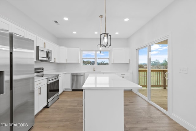 kitchen featuring appliances with stainless steel finishes, light wood-type flooring, pendant lighting, a center island, and white cabinetry