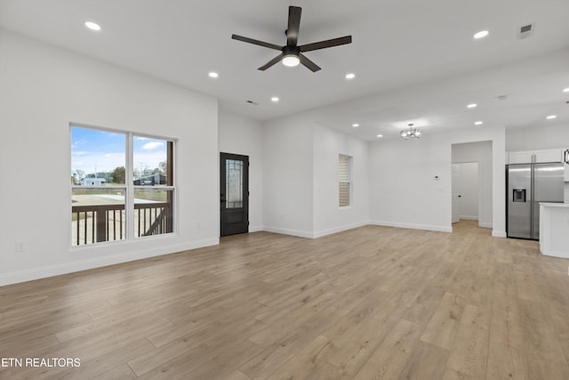 unfurnished living room with ceiling fan with notable chandelier and light wood-type flooring