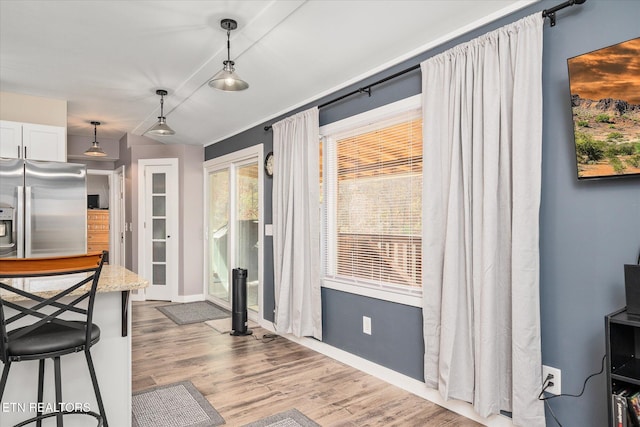 kitchen with stainless steel fridge, white cabinetry, hardwood / wood-style floors, and hanging light fixtures