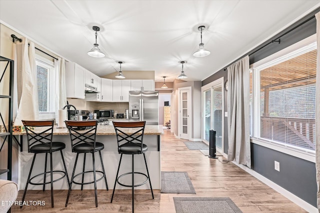 kitchen featuring stainless steel appliances, white cabinetry, hanging light fixtures, and light stone counters