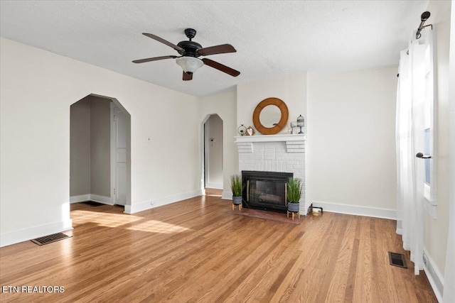 unfurnished living room featuring a brick fireplace, ceiling fan, a textured ceiling, and light hardwood / wood-style flooring