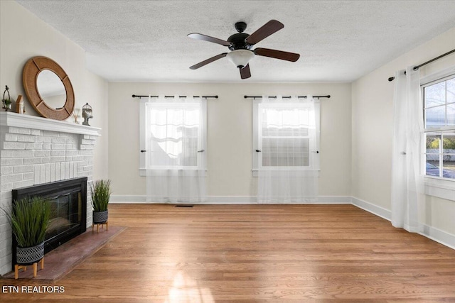 living room with ceiling fan, light hardwood / wood-style floors, a textured ceiling, and a brick fireplace