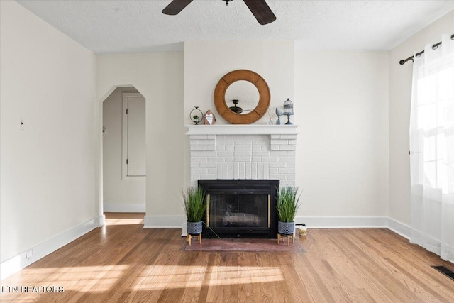 unfurnished living room featuring ceiling fan, a fireplace, wood-type flooring, and a textured ceiling