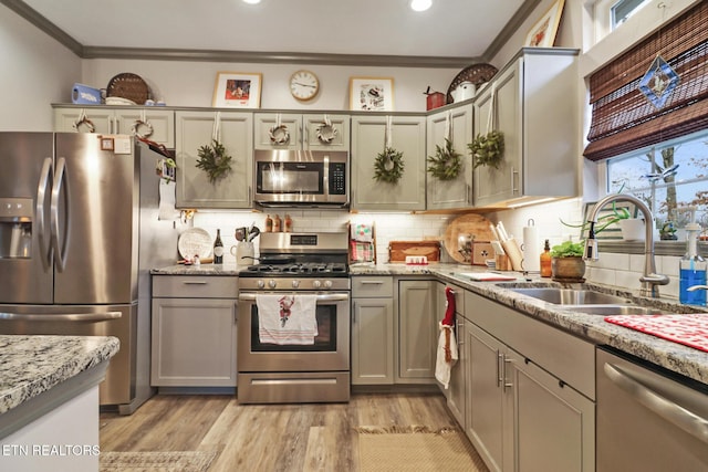 kitchen with light stone countertops, stainless steel appliances, crown molding, sink, and light hardwood / wood-style floors