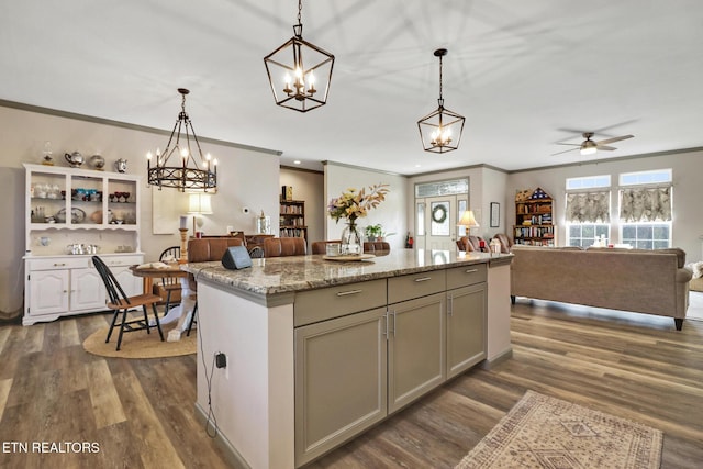 kitchen featuring a kitchen island, dark hardwood / wood-style floors, pendant lighting, ornamental molding, and light stone countertops