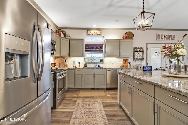 kitchen with sink, pendant lighting, stainless steel appliances, light stone countertops, and backsplash