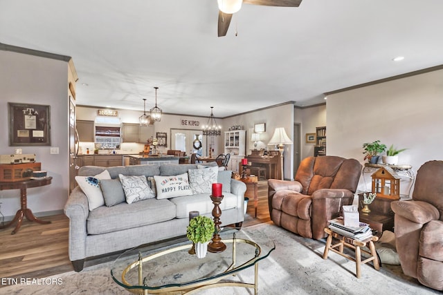 living room with ceiling fan with notable chandelier, ornamental molding, and light hardwood / wood-style floors