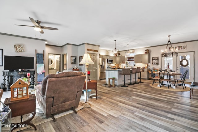 living room featuring hardwood / wood-style flooring, crown molding, and ceiling fan with notable chandelier