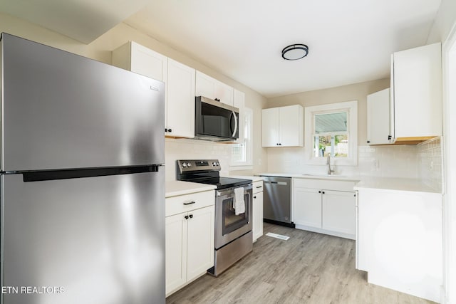 kitchen featuring decorative backsplash, light wood-type flooring, stainless steel appliances, sink, and white cabinetry