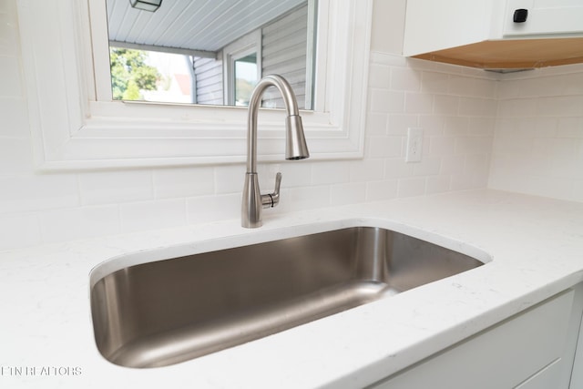 interior details with white cabinets, decorative backsplash, light stone countertops, and sink