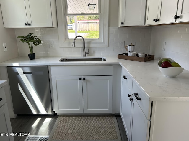 kitchen featuring white cabinets, a sink, backsplash, stainless steel dishwasher, and light stone counters