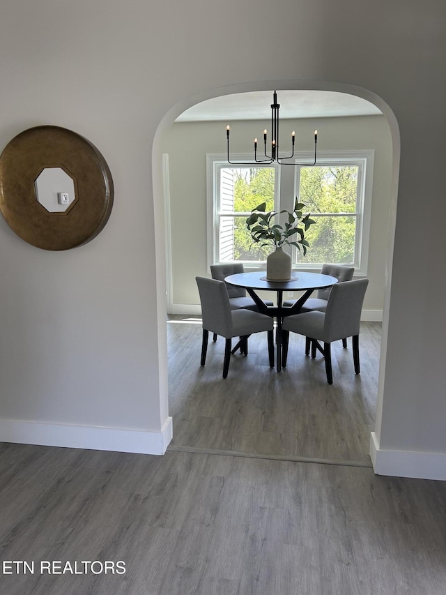 dining space with arched walkways, a notable chandelier, baseboards, and wood finished floors