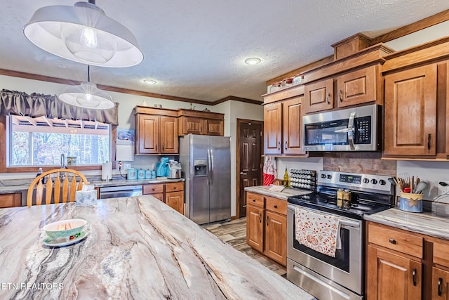 kitchen with decorative light fixtures, crown molding, light stone countertops, and stainless steel appliances