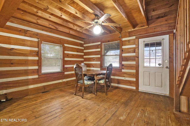 unfurnished dining area with ceiling fan, wood-type flooring, and wood walls