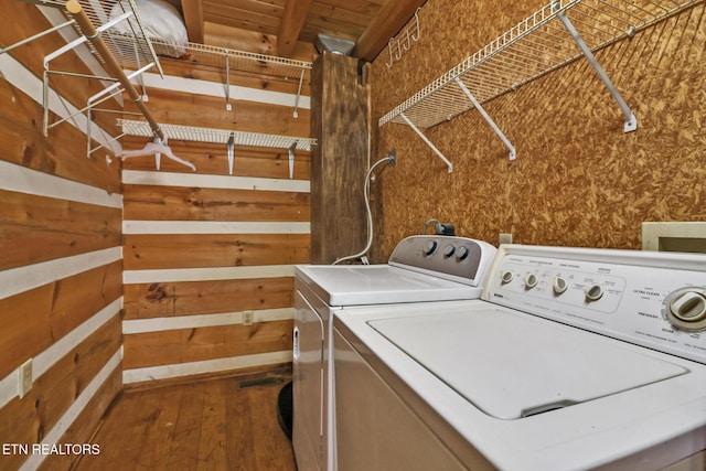 clothes washing area featuring washer and clothes dryer, wood-type flooring, and wood walls