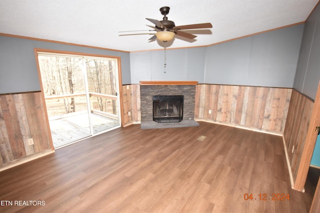 unfurnished living room featuring hardwood / wood-style flooring, ceiling fan, ornamental molding, and wood walls