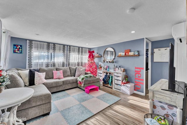 living room with a wall unit AC, light hardwood / wood-style flooring, and a textured ceiling