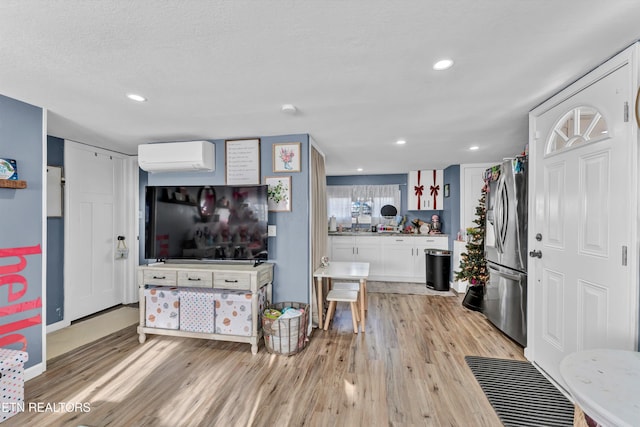 kitchen with white cabinetry, stainless steel fridge with ice dispenser, light hardwood / wood-style flooring, a wall unit AC, and a textured ceiling