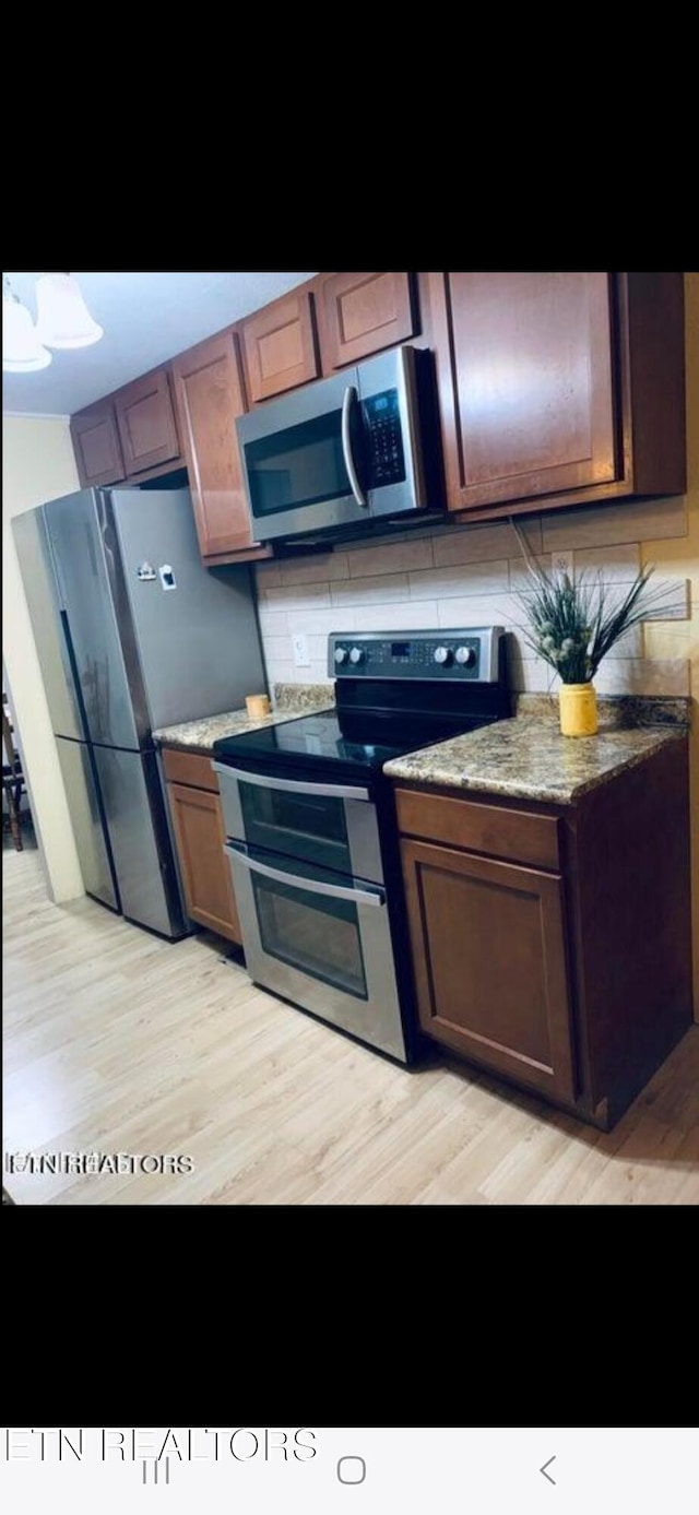 kitchen featuring appliances with stainless steel finishes, light wood-type flooring, stone counters, and tasteful backsplash