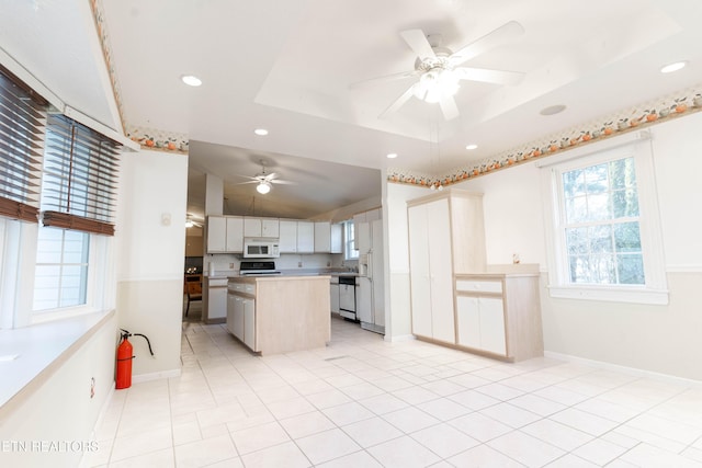 kitchen featuring white appliances, light tile patterned floors, a tray ceiling, a kitchen island, and white cabinetry