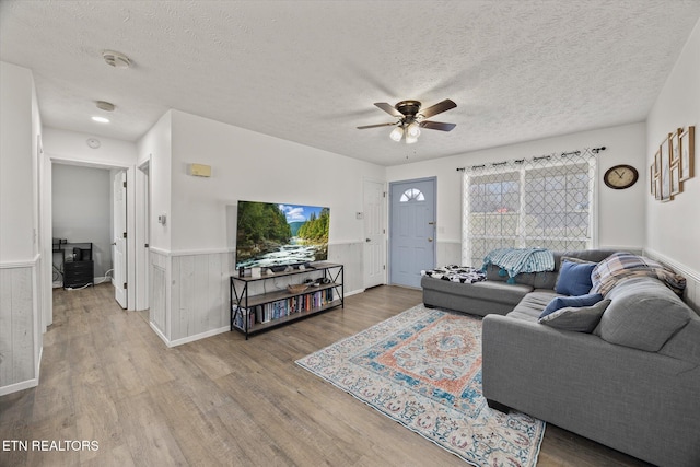 living room with hardwood / wood-style flooring, ceiling fan, wood walls, and a textured ceiling