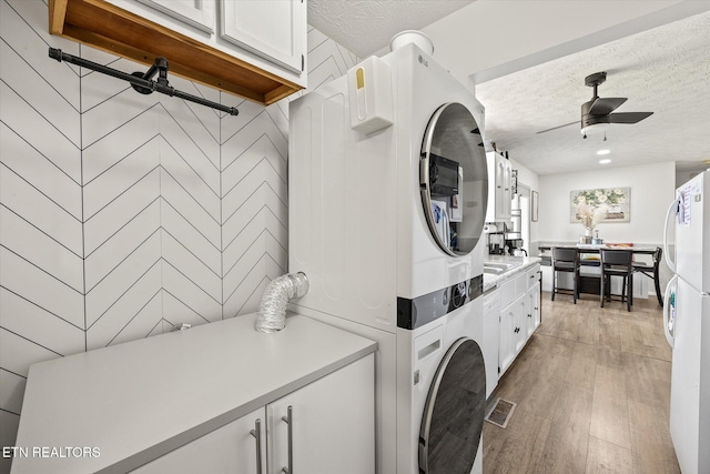 laundry area featuring light wood-type flooring, stacked washing maching and dryer, a textured ceiling, ceiling fan, and wood walls