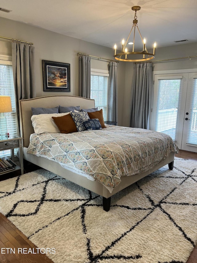 bedroom featuring access to exterior, french doors, hardwood / wood-style flooring, and a chandelier