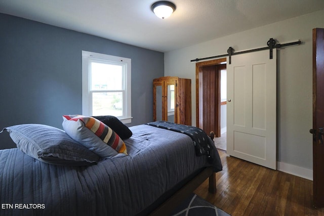 bedroom with a barn door and dark wood-type flooring