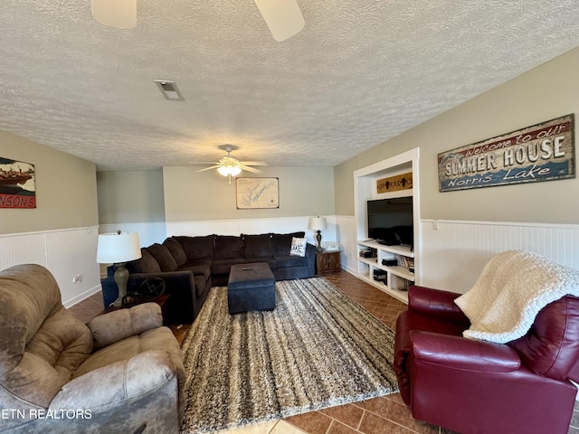 living room with ceiling fan, built in shelves, dark tile patterned floors, and a textured ceiling