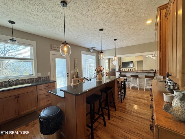 kitchen with hanging light fixtures, wood-type flooring, a breakfast bar, and sink