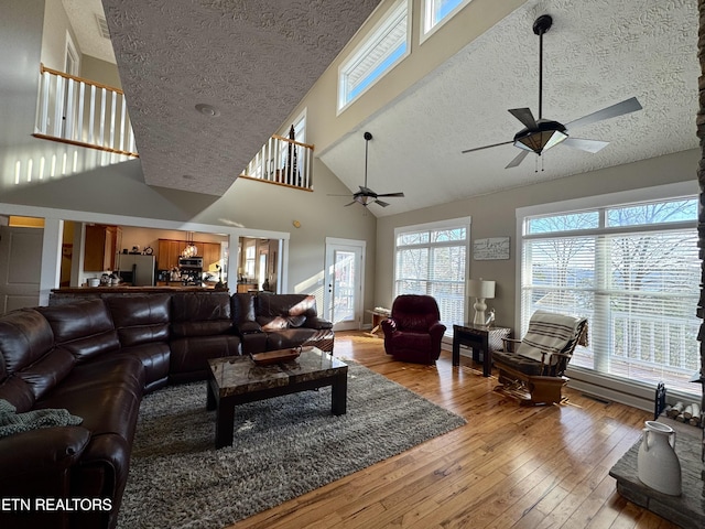 living room featuring a textured ceiling, ceiling fan, light hardwood / wood-style flooring, and high vaulted ceiling