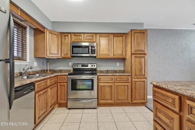 kitchen with light tile patterned floors, stainless steel appliances, light stone counters, and sink