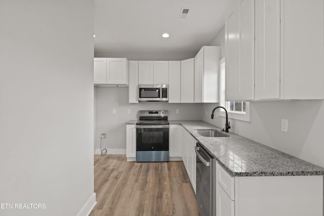 kitchen with white cabinetry, light stone countertops, stainless steel appliances, and a sink