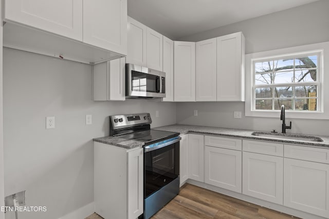 kitchen featuring a sink, wood finished floors, white cabinetry, appliances with stainless steel finishes, and light stone countertops