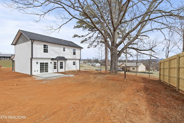 back of property with dirt driveway, a patio area, and fence