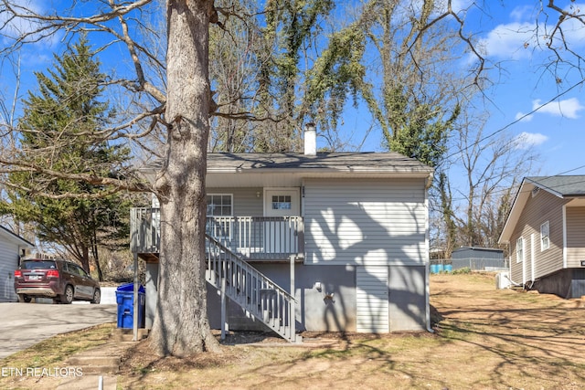 rear view of property with covered porch, a chimney, concrete driveway, and stairs