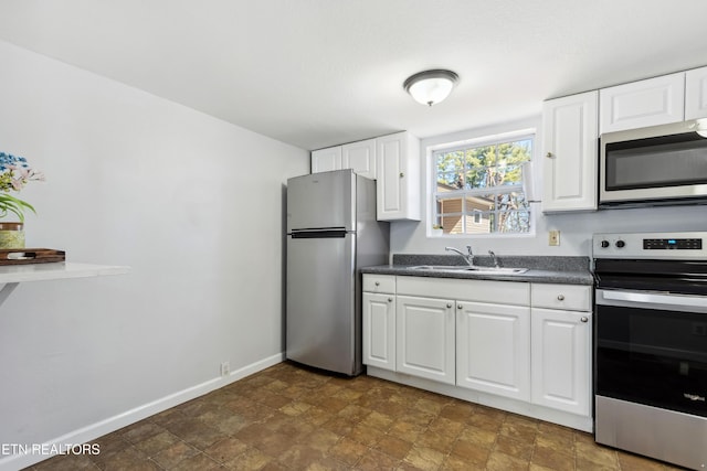 kitchen featuring dark countertops, appliances with stainless steel finishes, white cabinetry, a sink, and baseboards