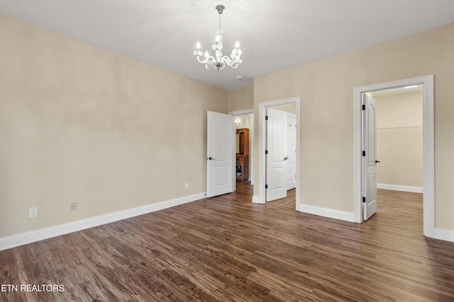 unfurnished bedroom with a closet, a spacious closet, dark wood-type flooring, and an inviting chandelier