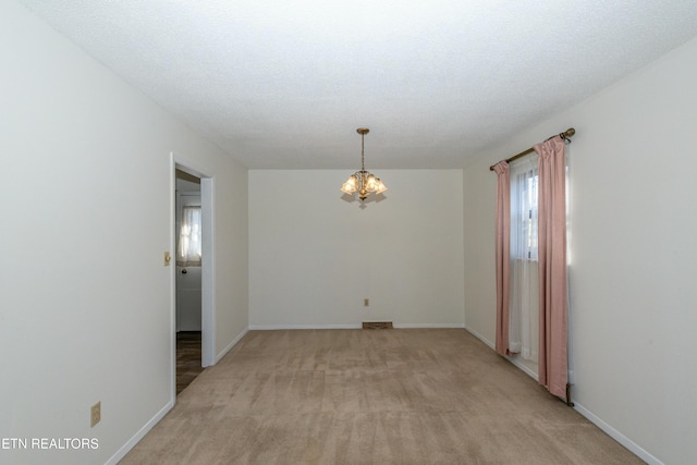 empty room with light colored carpet, a textured ceiling, and a notable chandelier