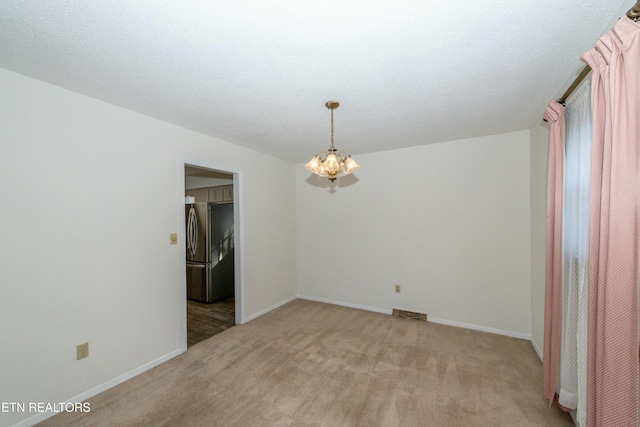 empty room with a textured ceiling, light carpet, and a chandelier