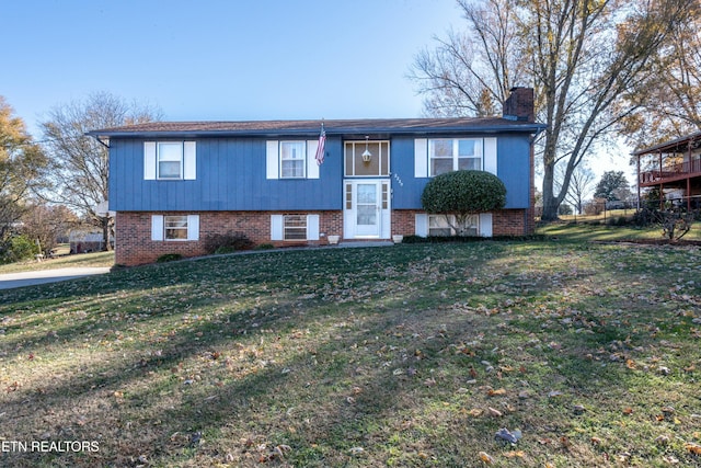 raised ranch with a chimney, a front lawn, and brick siding