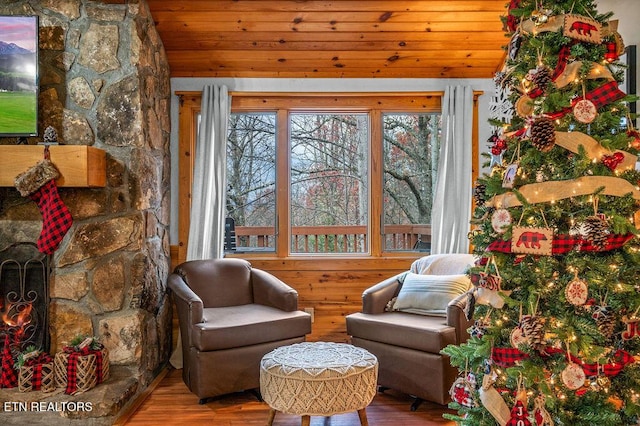 living area with hardwood / wood-style flooring, a stone fireplace, and wood ceiling