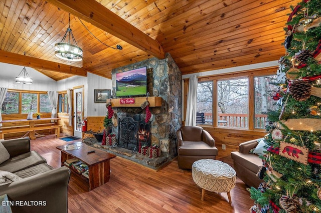 living room with vaulted ceiling with beams, wooden walls, a stone fireplace, and wood-type flooring