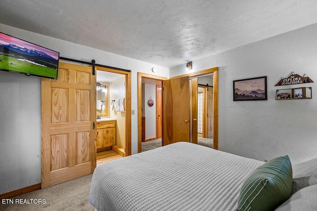 bedroom with connected bathroom, a barn door, and carpet