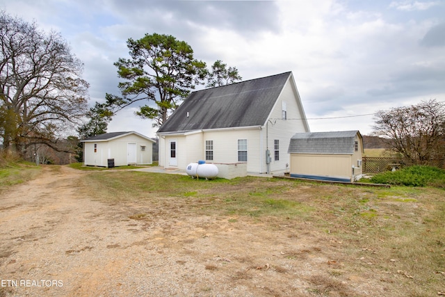 back of house with a storage unit, a shingled roof, and an outdoor structure