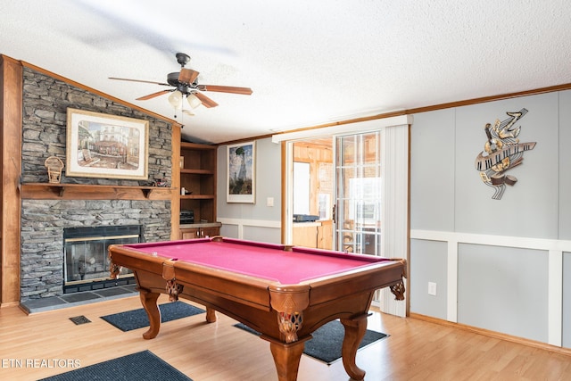 playroom featuring a stone fireplace, pool table, a textured ceiling, and hardwood / wood-style flooring