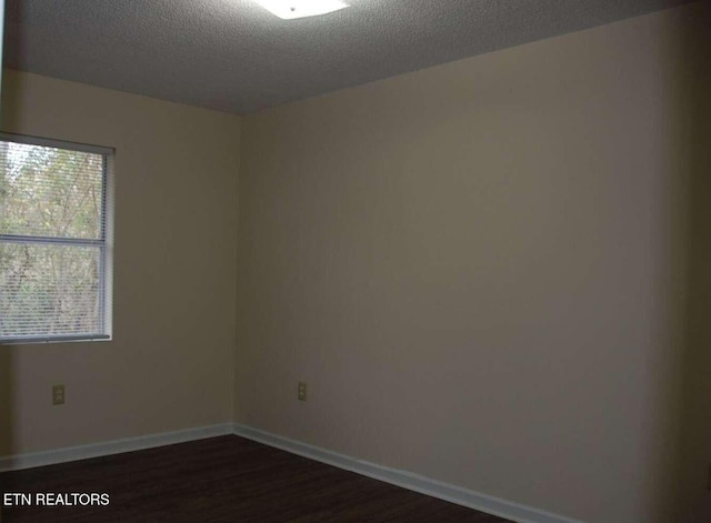 empty room with a textured ceiling and dark hardwood / wood-style floors